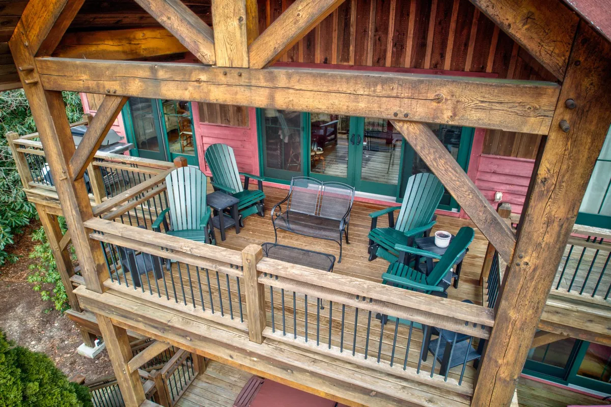An exterior deck scene with sturdy wooden beams, Adirondack chairs, a metal bench, and a wooden railing, all set against a backdrop of lush greenery. It evokes a sense of relaxation and invites guests to enjoy morning coffee or evening stargazing while taking in mountain air.
