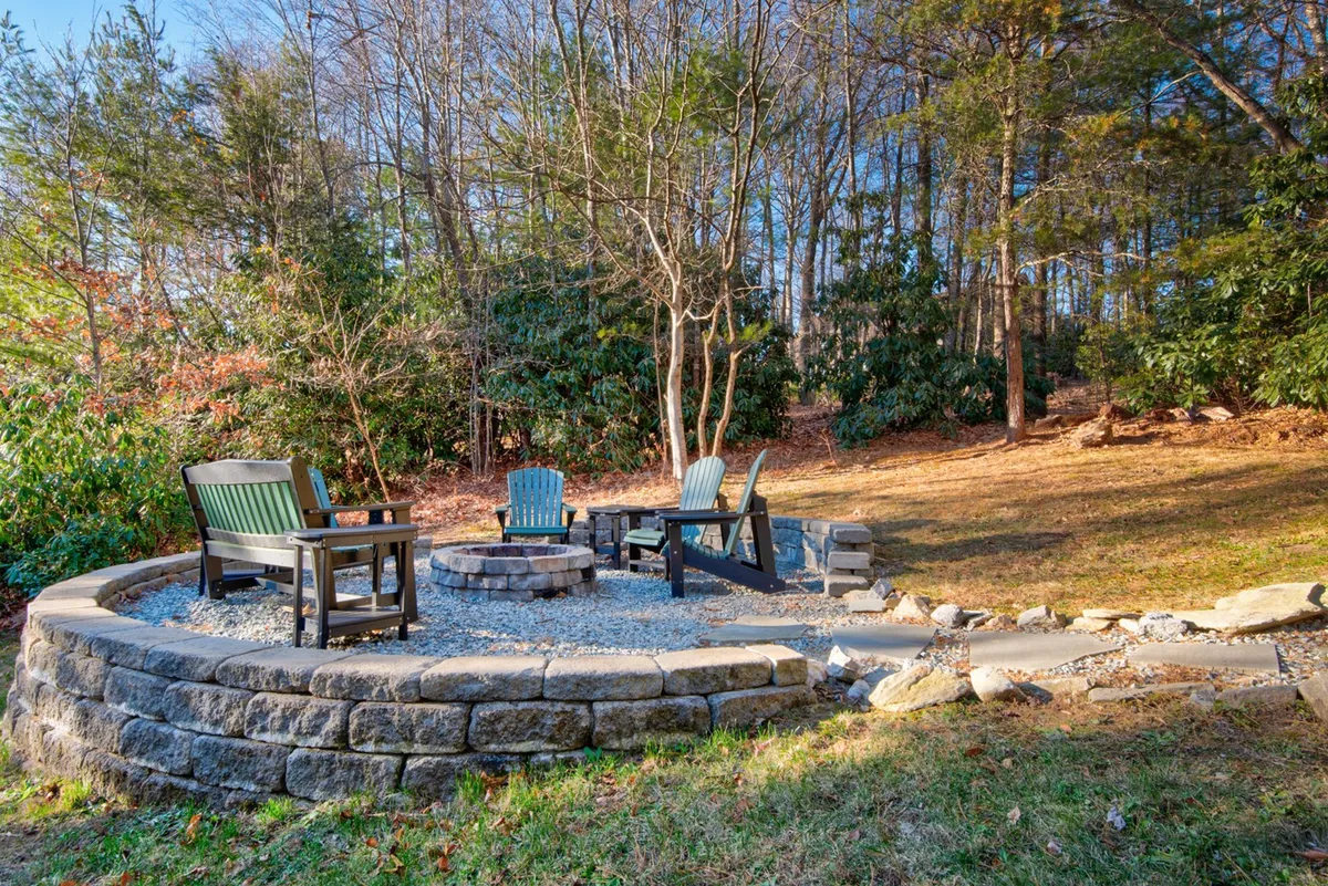 A closeup of the fire pit area, surrounded by Adirondack chairs and dense woodland. The setting is intimate yet open, making it an ideal spot to unwind, socialize, and enjoy nature after exploring nearby dog-friendly trails.