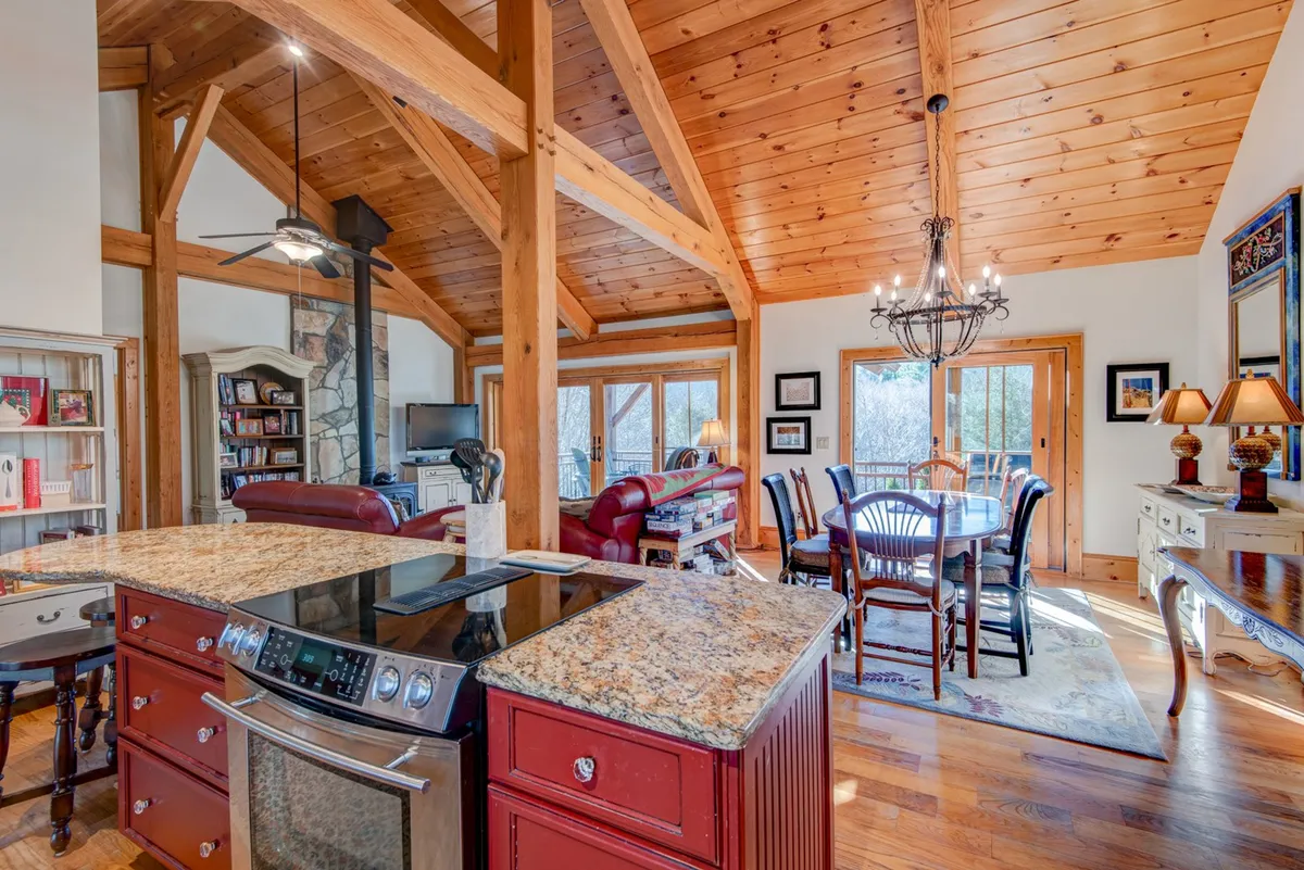 A warm, open-concept layout featuring a kitchen with granite countertops and wooden beams, a spacious dining table, and a living area with a cozy leather sofa. The space is designed for seamless group gatherings and relaxing evenings.