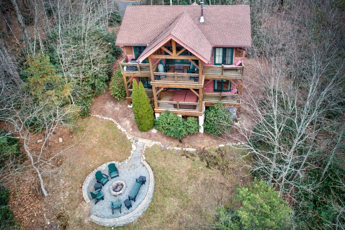 The image showcases a large wooden cabin nestled among trees, with an inviting fire pit area and expansive deck. The setting evokes feelings of cozy evenings spent outdoors, stargazing, or recounting adventures by the fire—an ideal environment for both people and pets.