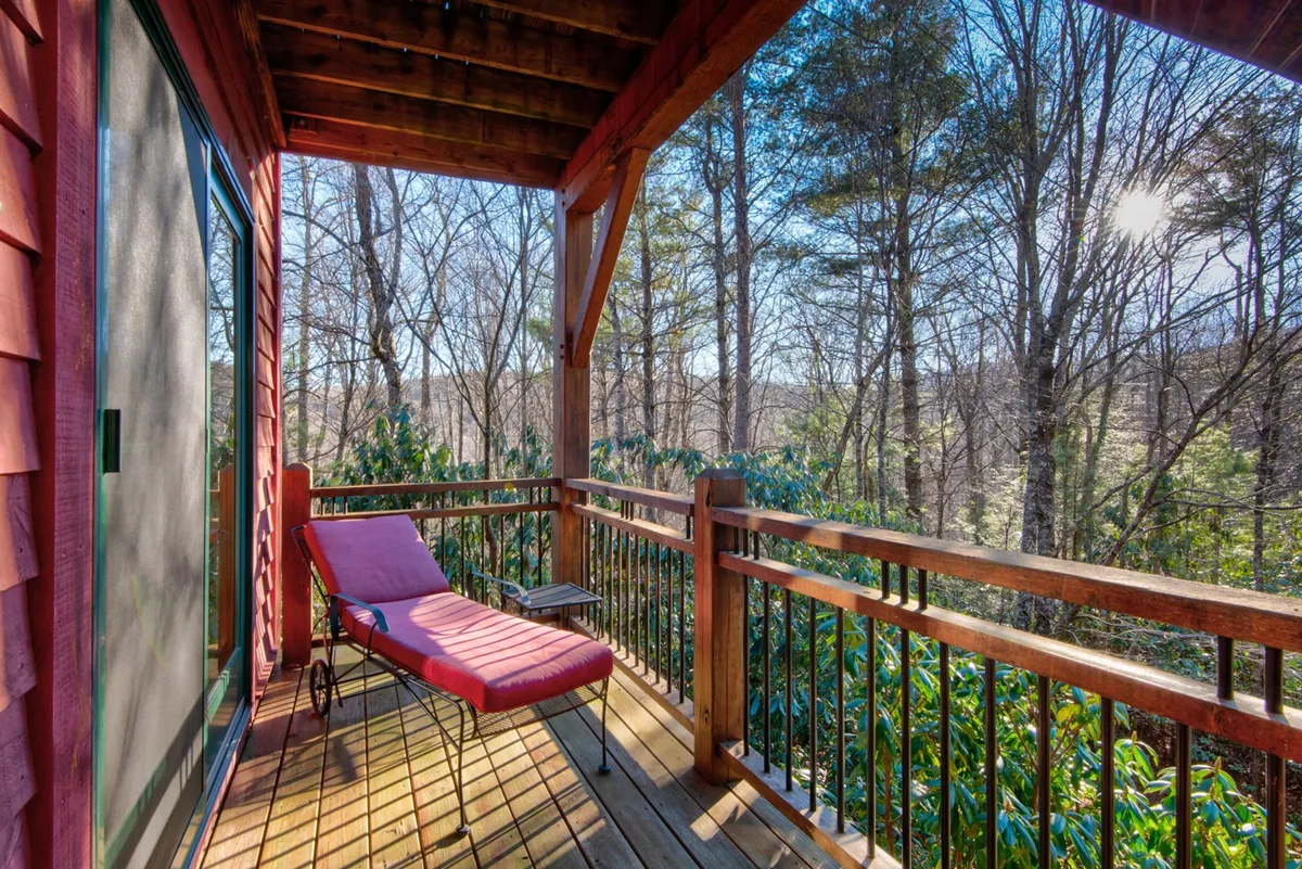 A peaceful deck with a red lounge chair set against wooden railings, surrounded by trees. The calm outdoor space invites moments of solitude or togetherness, perfect for sipping morning coffee, reading, or stargazing at night in the fresh mountain air.