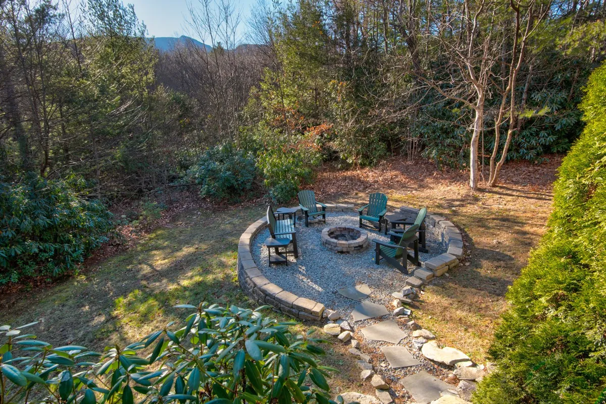 A rustic outdoor fire pit area, encircled by Adirondack chairs, sits amid lush greenery and a stone pathway. The scene invites guests to gather, share stories, or stargaze after a day spent discovering local parks and trails.