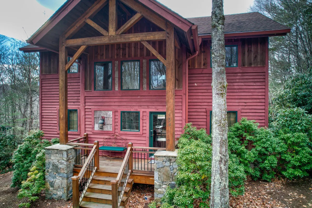 The inviting exterior of Muir Lodge, showcasing its striking red façade, exposed wooden beams, stone steps, and surrounding lush greenery. The perspective hints at the architectural elegance and tranquil setting, with the lodge nestled harmoniously within its natural environment.